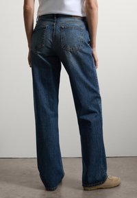 Jeans in denim blu a gamba larga con vita alta, dotati di due tasche posteriori e taglio dritto. Il tessuto presenta una texture leggermente sbiadita.
