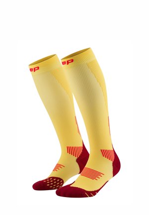 Compression socks featuring a yellow body with red accents, ribbed texture, and patterned footbed for enhanced grip and support.