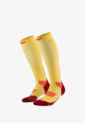 Compression socks featuring a yellow body with red accents, ribbed texture, and patterned footbed for enhanced grip and support.