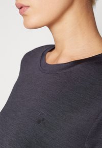 Dark gray athletic shirt with a round neckline, smooth texture, and a small, black logo on the chest area. Simple and fitted design.