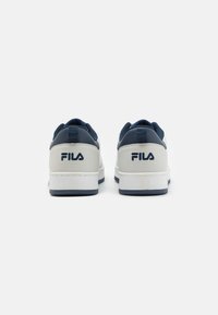 Sneaker bianche e blu navy con una finitura in pelle liscia, dotate di colletto imbottito, dettagli testurizzati e logo Fila sul tallone.