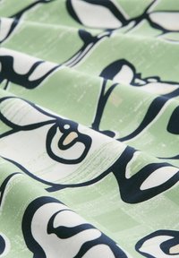 Tissu en coton avec une texture lisse et mate, présentant un fond vert. De grands motifs floraux abstraits en bleu marine créent un intérêt visuel.