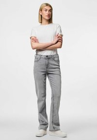 Pelēki džinsi ar taisno kāju griezumu, 5 kabatām, priekšējo pogu un rāvējslēdzēja aizdari, kombinēti ar vienkāršu baltu T-kreklu un baltiem sporta apaviem.