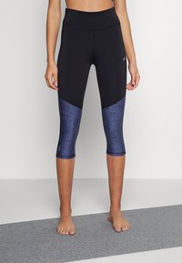 Leggings Capri noirs en matériau extensible, avec un accent texturé bleu au bas des jambes et une taille haute.