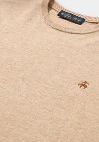 Maglione beige a maglia con scollatura rotonda e bordi a costine. Presenta un piccolo logo ricamato marrone sul petto. Texture morbida.