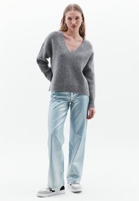 Maglione grigio a coste con scollatura a V, abbinato a pantaloni ampi lucidi di un azzurro chiaro e sneaker grigie con dettagli neri.