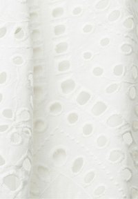 Tissu blanc avec un motif brodé à jours comprenant des découpes circulaires et ovales disposées dans un dessin décoratif et répétitif.