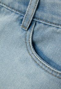 Tela de mezclilla azul claro que presenta un primer plano de un área de bolsillo, con costuras visibles y una superficie texturizada.