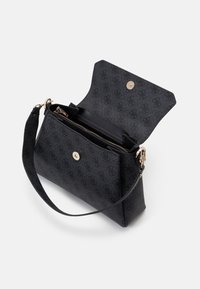 Sac à épaule noir à motifs avec rabat ouvert montrant un compartiment zippé et une fermeture magnétique dorée, sangle détachable sur fond blanc.