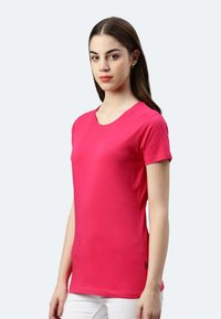 T-shirt rosa a maniche corte realizzato in tessuto morbido, con scollo rotondo, un design aderente e un piccolo logo sul lato.