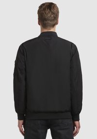 Schwarze Bomberjacke mit einer glatten, matten Oberfläche. Verfügt über einen gerippten Kragen und Bündchen, Seitentaschen und kontrastierende Nähte entlang der Nähte.