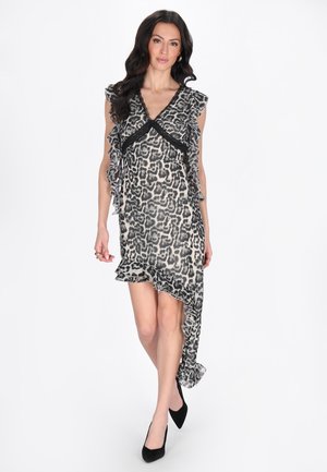 Vrouw draagt een mouwloze zwarte en grijze leopardprintjurk met ruches en een asymmetrische zoom, gecombineerd met zwarte hakken.