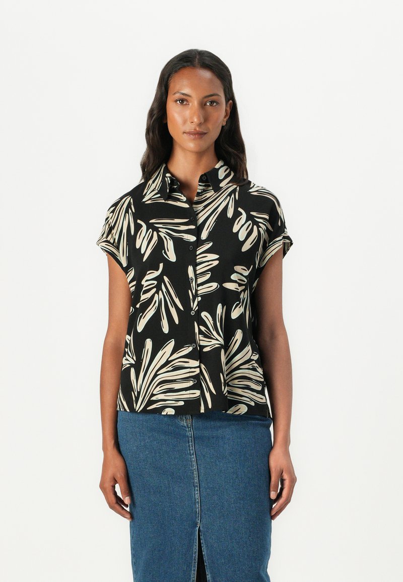 Kortebloezem zwart shirt met witte bladdessin, een knoopsluiting aan de voorkant en een gespreide kraag, gecombineerd met een blauwe denimrok.