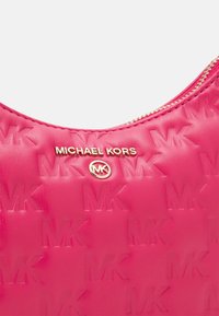 Różowa skórzana torebka na ramię z wytłoczonym wzorem logo MK, złotymi akcentami i zapięciem na zamek u góry.