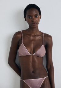 Roze lingerieset met een driehoekige bralette en bijpassende thong. Gemaakt van soepel materiaal met dunne bandjes en subtiele hardware-accenten.