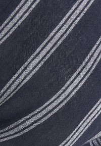 Tessuto blu marina con strisce bianche diagonali. Il materiale appare strutturato, con una finitura morbida e tessuta. Le strisce variano in spessore.