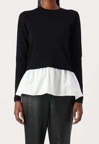 Czarny dzianinowy top z długimi rękawami i obszytą białą warstwą peplum. Top ma okrągły dekolt i jest zestawiony z czarnymi skórzanymi spodniami.