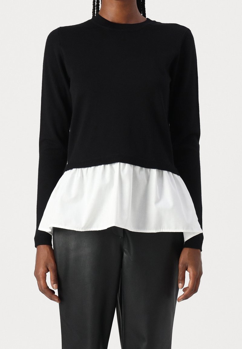 Czarny dzianinowy top z długimi rękawami i obszytą białą warstwą peplum. Top ma okrągły dekolt i jest zestawiony z czarnymi skórzanymi spodniami.