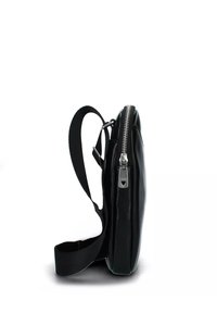Borsa nera in pelle con un profilo sottile, dotata di cerniera in argento e tracolla regolabile. Il design è minimalista e moderno.
