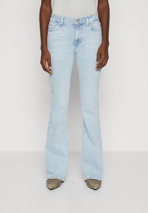 Jean flare bleu clair en denim doux, avec un design à cinq poches et une taille mi-haute. Porté avec des chaussures à bout pointu.