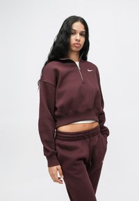 Maroon cropped collegepaita, jossa on vetoketju, ribbaa hihansuissa ja valkoinen logo-aksentti. Yhdistetty samanvärisiin maroon-housuihin, joissa on elastinen vyötärö.