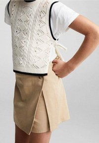 Top senza maniche lavorato a maglia bianco con motivi testurizzati e bordi neri, abbinato a una mini gonna beige con uno spacco laterale.