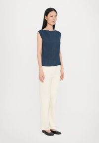 Navy ribbelvrije top zonder mouwen met een vierkante hals, gecombineerd met crèmekleurige brede broek en zwarte flats. Soepele textuur en casual pasvorm.