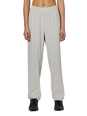 Person trägt locker sitzende, hellgraue Hosen mit elastischem Bund und schwarze, geschnürte Sportschuhe, steht vor einem weißen Hintergrund.