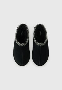 Black suede slippers with a soft interior, featuring a stitched, textured border at the opening. Rounded toe and low-profile design.