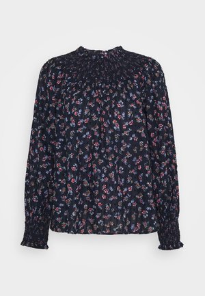 Blouse bleu foncé à manches longues avec un petit imprimé floral rouge, violet et blanc, col montant smocké et poignets, coupe ample.