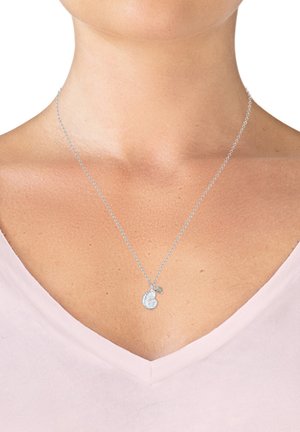 Silver necklace featuring a textured, circular pendant with intricate detailing and a small bow accent, worn with a light pink v-neck top.