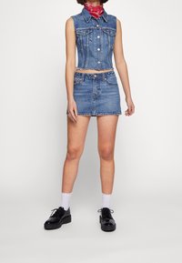 Jeans ärmlös jacka i kombination med en högmidjad denimkjol. Ljusblå, blekt textur med metallknappar och framfickor. Svarta platåskor.