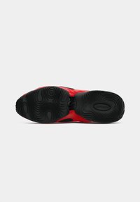 Zapatilla deportiva roja con una suela de goma negra con un patrón ondulado, material superior suave y áreas de ventilación prominentes.