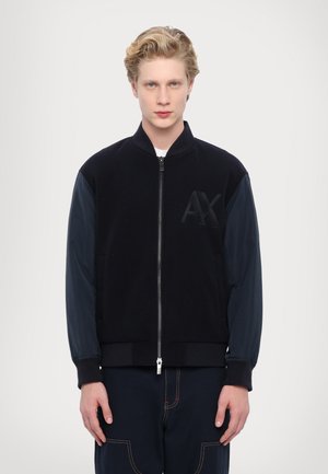 Giubbotto bomber nero con maniche blu navy, chiusura con zip, polsini a coste, tessuto strutturato, con logo AX in rilievo sulla parte anteriore.