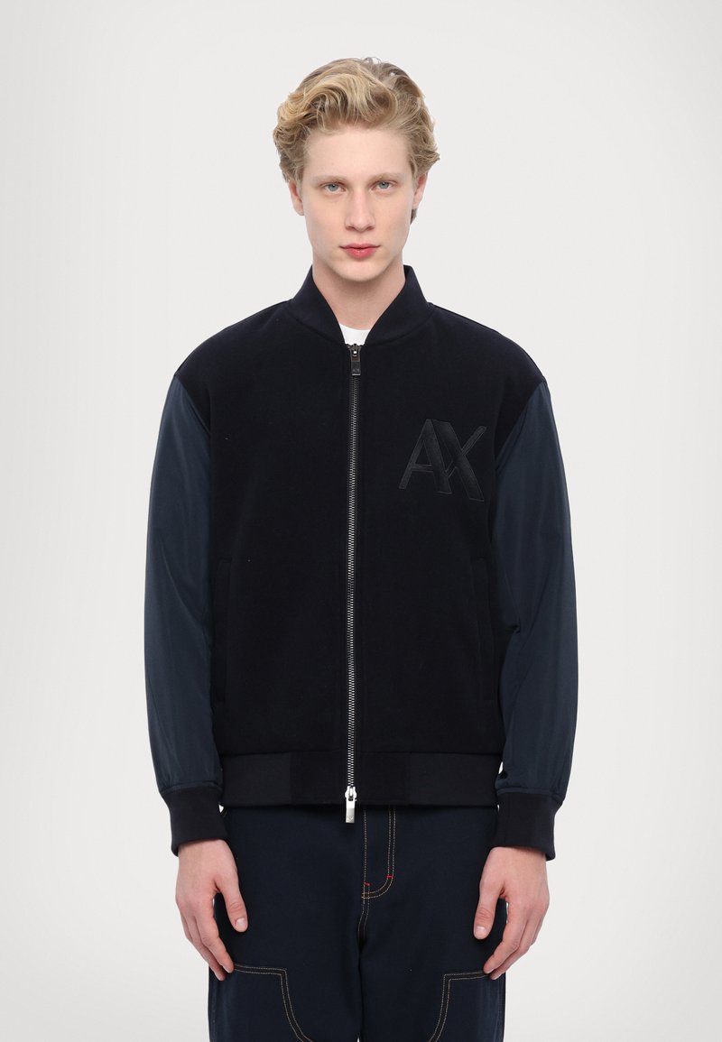 Giubbotto bomber nero con maniche blu navy, chiusura con zip, polsini a coste, tessuto strutturato, con logo AX in rilievo sulla parte anteriore.