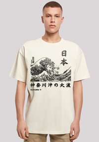 Cream-colored cotton t-shirt featuring a black wave graphic and Japanese text. Short sleeves and a relaxed fit. No visible logos.
