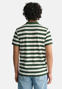Polo de rayas verdes y blancas con un cuello clásico, mangas cortas y un corte relajado. Mostrado desde la parte de atrás, exhibiendo el diseño y la textura.