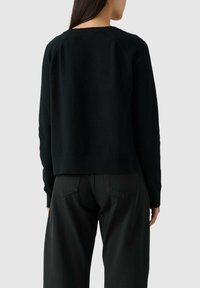 Maglione nero lavorato a maglia con scollatura tonda e orlo a coste, caratterizzato da una vestibilità rilassata e una lunghezza leggermente accorciata.