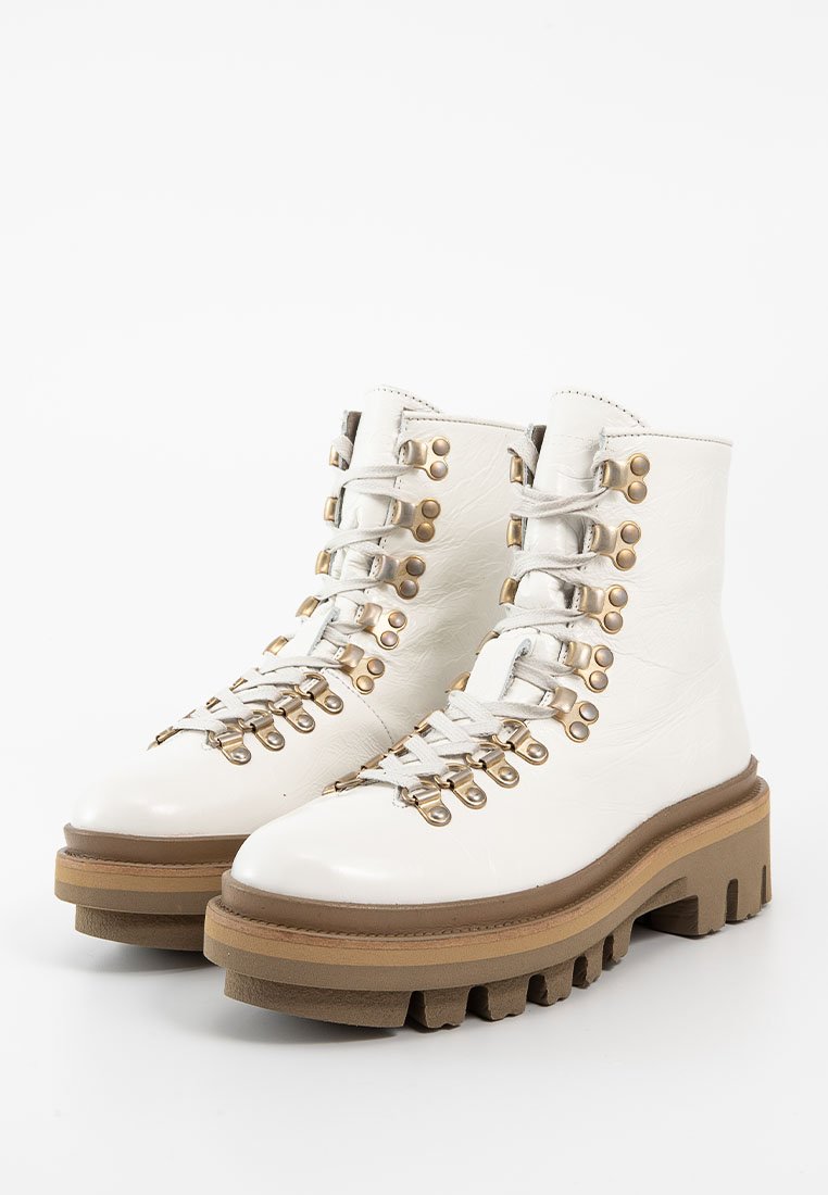 Weiße Leder-Ankle-Boots mit einer dicken braunen Gummisohle, ausgestattet mit goldenen Verzierungen und Schnürsenkeln, strukturierter Oberfläche und runder Zehenform.