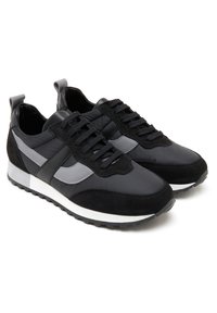 Schwarze Sportschuhe aus einer Mischung aus glattem Leder und Wildleder. Sie haben eine strukturierte Oberfläche, graue Akzente und eine weiße Außensohle.