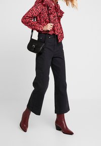 Red leopard print blouse with ruffled collar, black high-waisted wide-leg jeans, black crossbody bag, and burgundy pointed toe ankle boots.