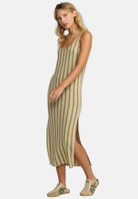 Vestido maxi de punto con rayas verticales en beige y verde, con aberturas laterales. Combinado con zapatos sin cordones de un tono crema claro. Textura suave y diseño ajustado.