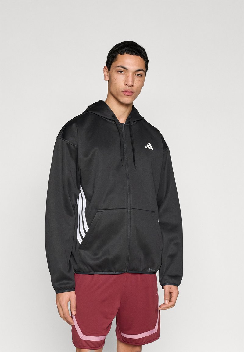 Sweat à capuche noir zippé en tissu lisse, avec un logo blanc sur la poitrine et trois bandes blanches le long des manches.