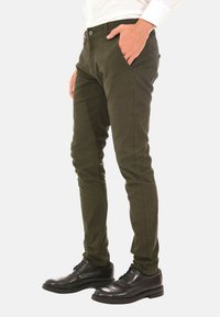 Pantaloni verde scuro, con texture e vestibilità slim, tasche frontali e chiusura con bottone, abbinati a scarpe eleganti nere.