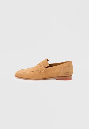Tanfarvet ruskind slip-on loafer med syningsdetalje på remmen og træsål, sidevisning på ensfarvet hvid baggrund.