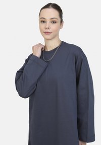 Přesně padnoucí oversized sweatshirt v námořnické modré barvě vyrobený z bavlny, s dlouhými rukávy a kulatým výstřihem. Obsahuje jemnou ribbovanou texturu a vrstvený stříbrný řetízek.