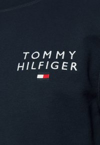 Sweatshirt en coton bleu marine avec logo brodé blanc "TOMMY HILFIGER" et un petit accent en tissu rouge, blanc et bleu.
