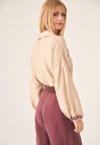 Blusa de corte holgado en color crema con mangas abullonadas y acentos bordados, combinada con pantalones burdeos de talle alto.