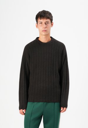 Suéter de color marrón oscuro con un escote redondo, mangas largas y un corte relajado, combinado con pantalones verdes. Textura suave y diseño sutil.