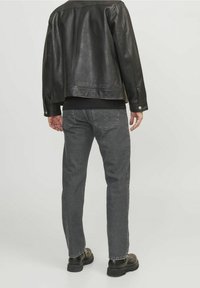 Chaqueta de cuero negro con una textura suave, combinada con jeans de mezclilla gris. Los jeans presentan un corte clásico y bolsillos traseros visibles.